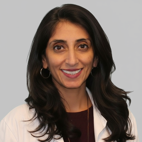 A woman with long, dark hair wearing a white lab coat and hoop earrings, smiling at the camera against a plain gray background.