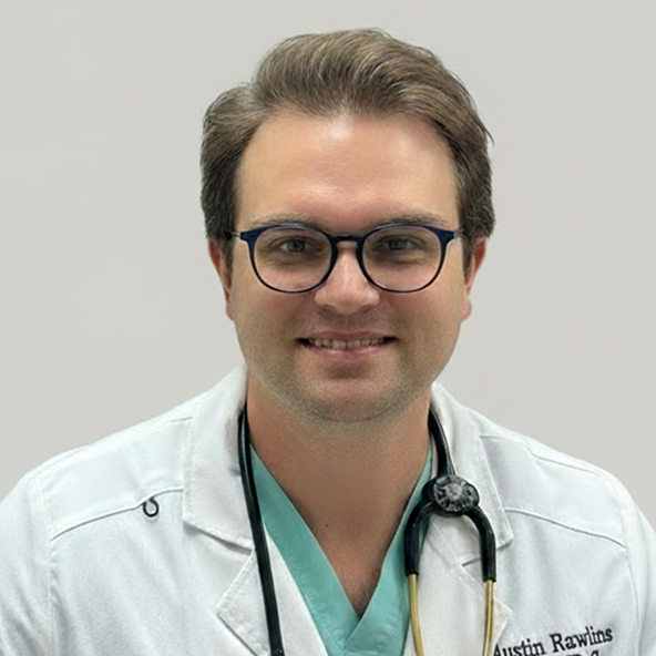 A man in medical attire with glasses and a stethoscope, smiling at the camera against a plain background.