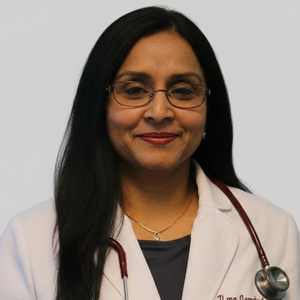 A woman with long black hair and glasses wears a white doctor's coat and a stethoscope around her neck, standing against a plain background.